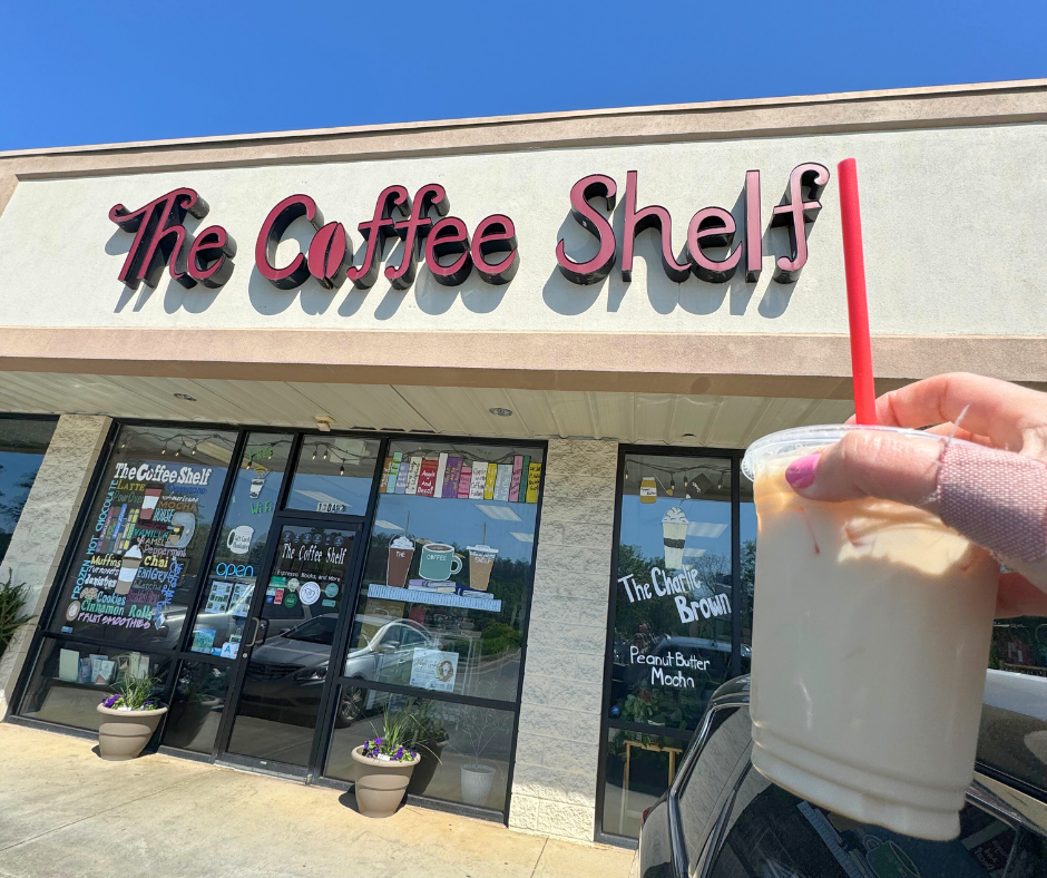 A fresh cup of coffee in front of The Coffee Shelf sign in Chapin, SC — a local favorite combining books and brews in a cozy café setting. - realtorlakemurraysc.com