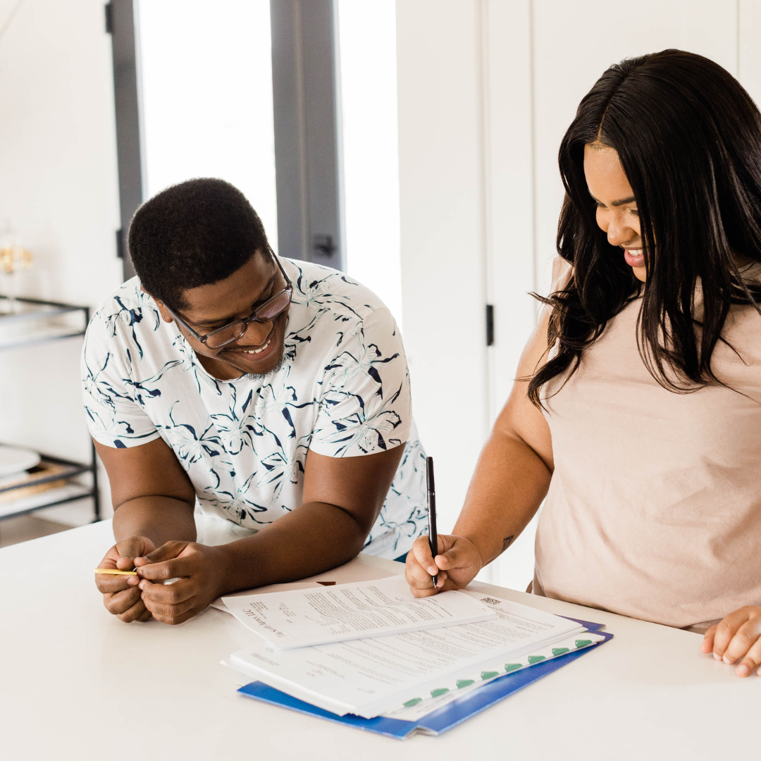 A couple smiling while signing contracts in a kitchen