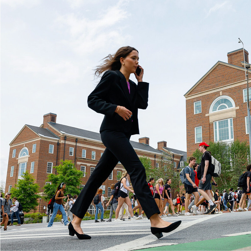 A female college student in a suit uses the cell phone while crossing the street