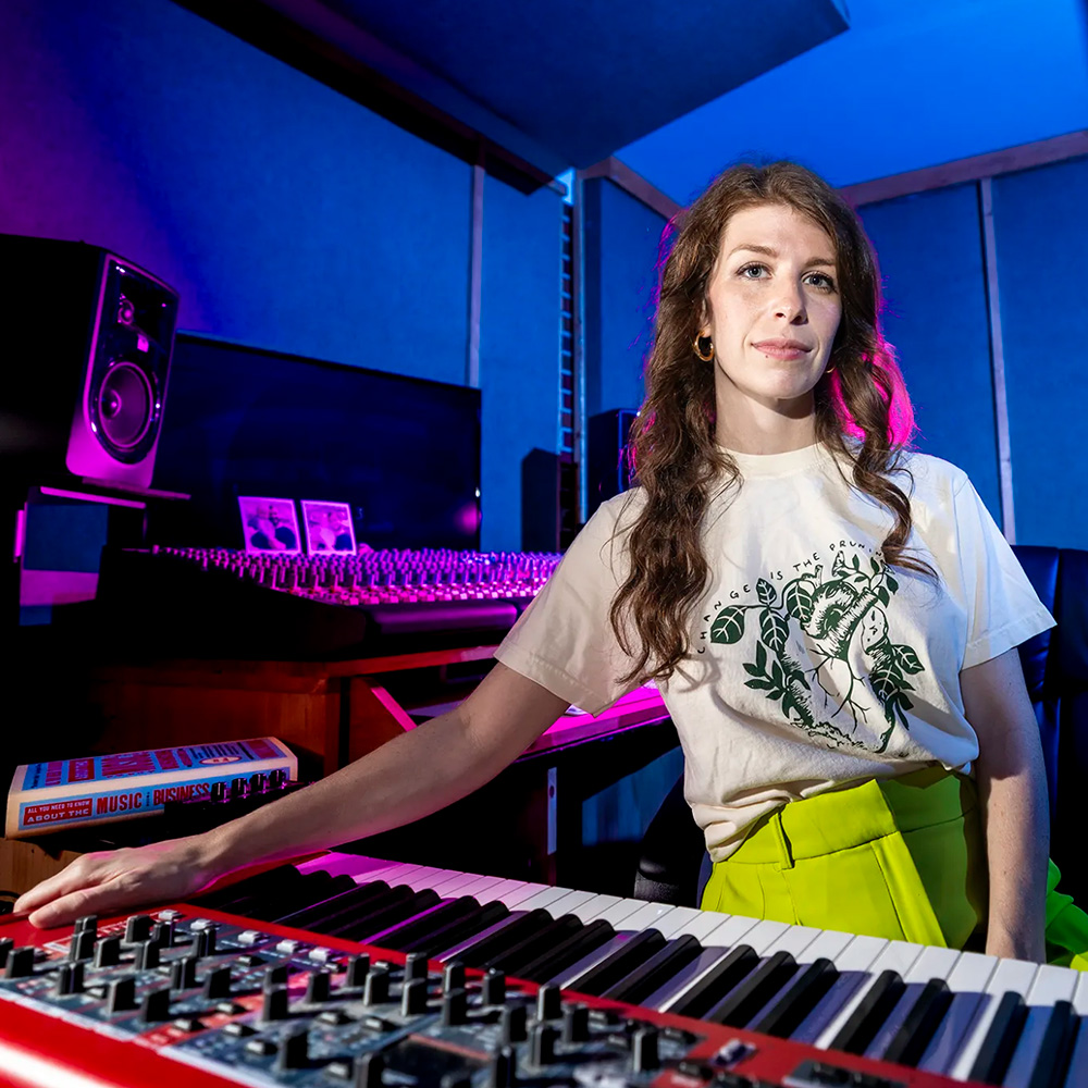 Lane Marie O'Kelley sits in front of a key board in a moodily-lit studio.