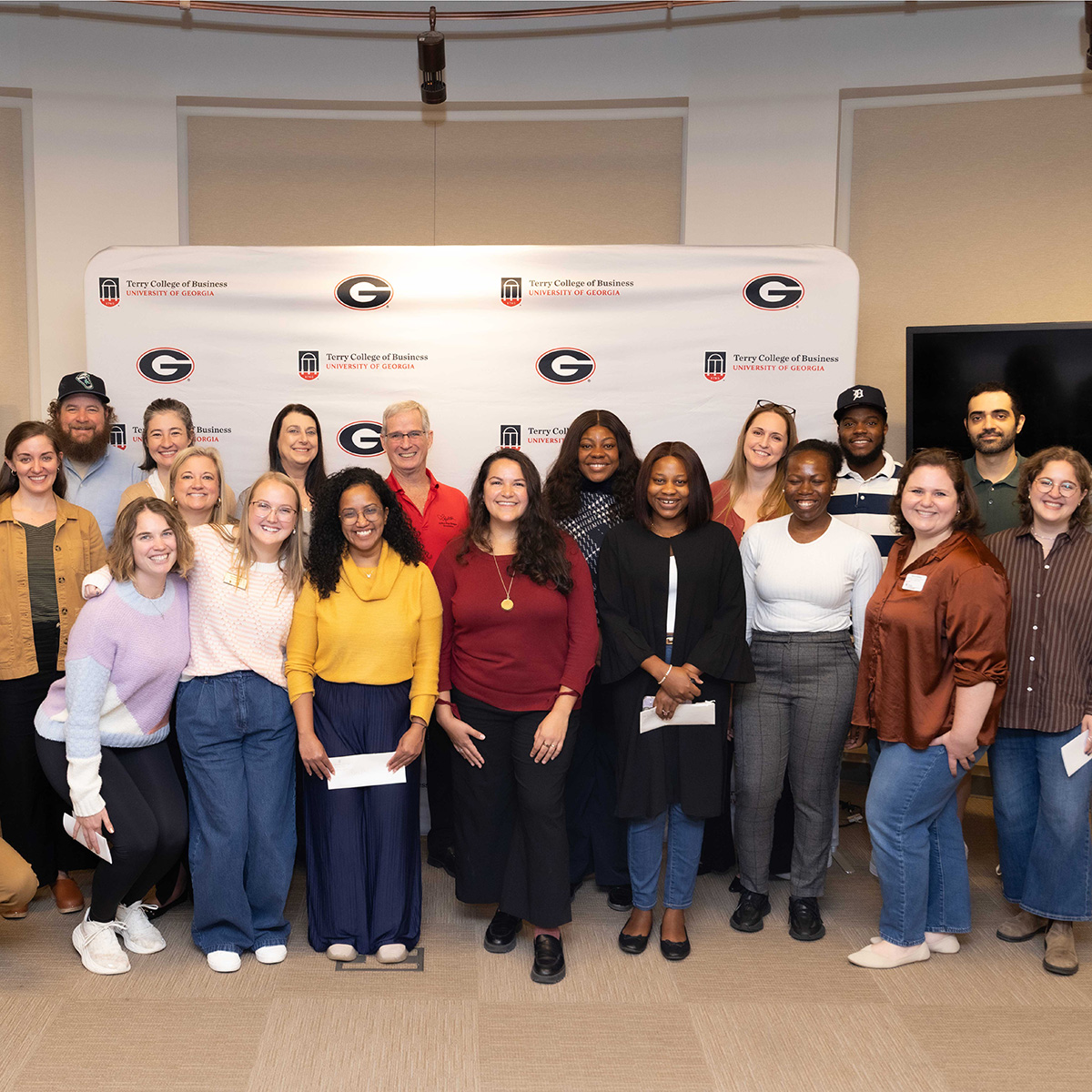 A crowd of MBA students posing with nonprofit leaders in front of a Terry College photo backdrop 