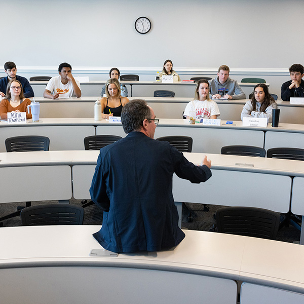 Neil Bendle sits on a desk while he teaches a marketing class