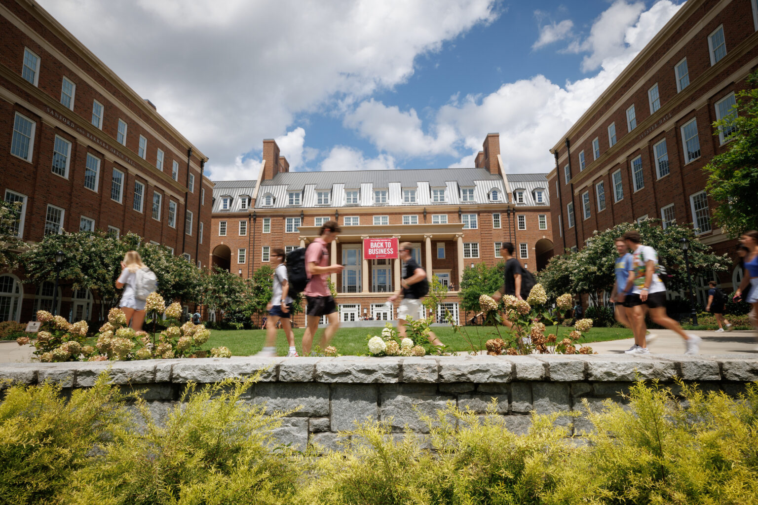 Corey Staughter poses with his arms crossed in a gray suit in front of a historic building on UGA's north campus. 