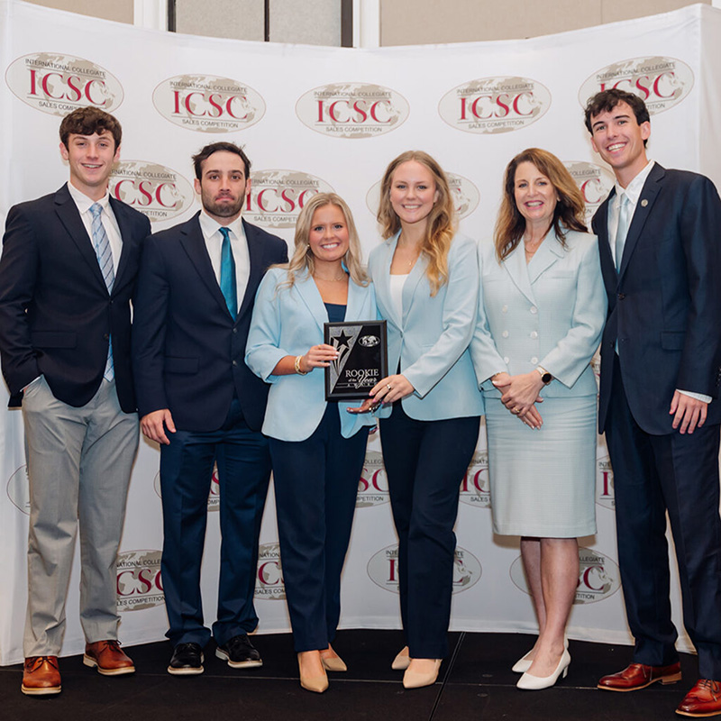 Sales students hold an awards plaque with instructor and coach Cindy Rippé 