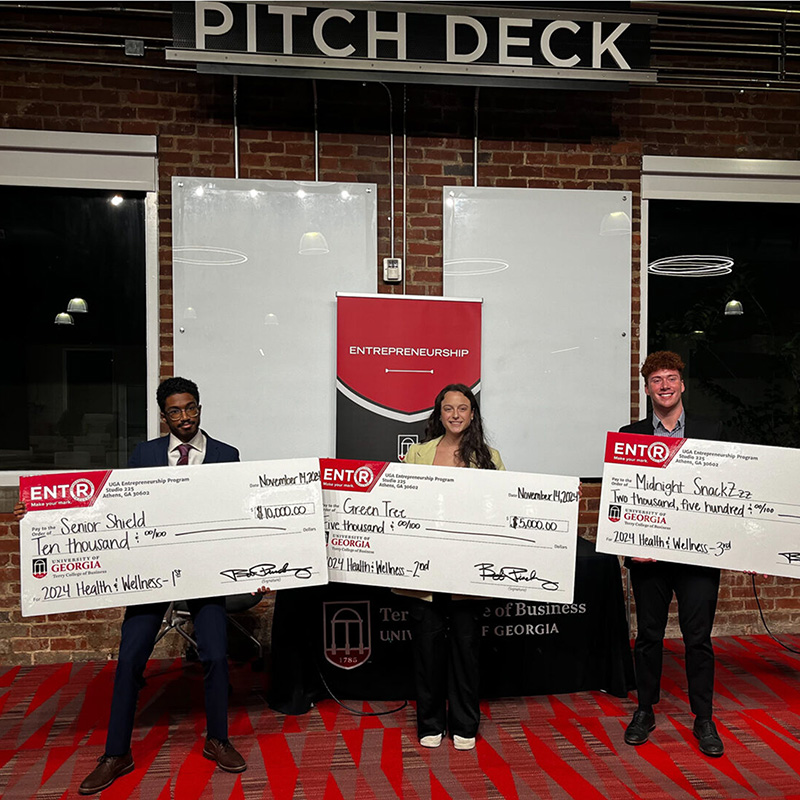 Kareem Elfoulie, Halle Greenbaum and Michael Hearnes stand in front of a sign that says pitch deck at Studio 225.