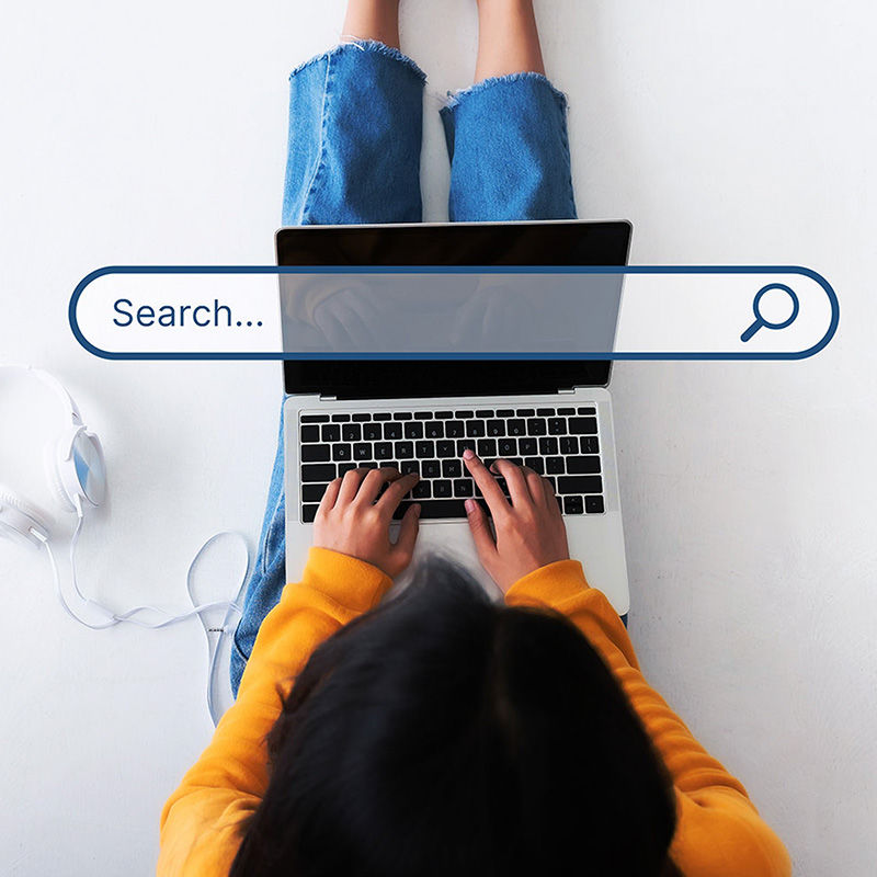 Woman sits with a laptop in her lap and searches the internet. 