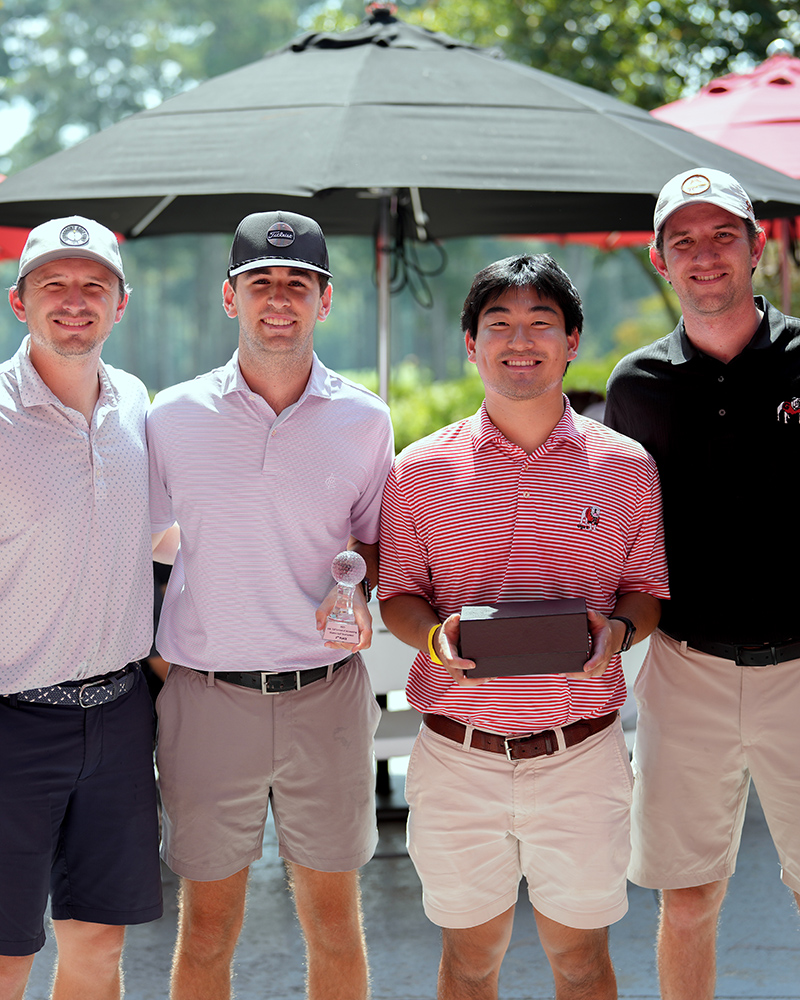Group photo of 4 male golfers. One golfer, 2nd from right, holds a trophy