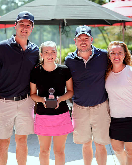 Margaret Christ with a group of golfers. A woman with pink shorts, 2nd from left, holds a trophy