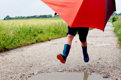 Person holding red umbrella leaping over puddle