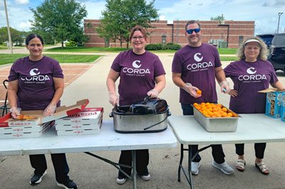 Corda employee volunteers standing behind food table, ready to serve