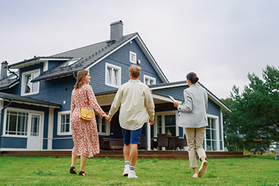 Couple holding hands walking toward a house with their real estate agent
