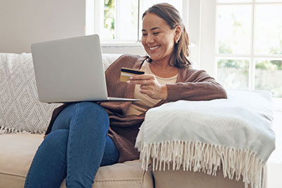 Woman sitting on the couch with her laptop and credit card in hand