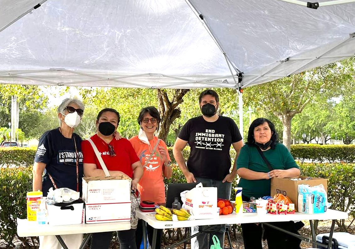 Five people stand behind a table with snacks and supplies  to support immigrants who attend check-ins with ICE.