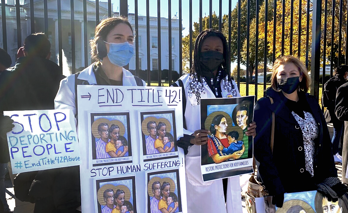 Several people stand in front of the White House in Washington, D.C., holding signs that read ''End Title 42''
