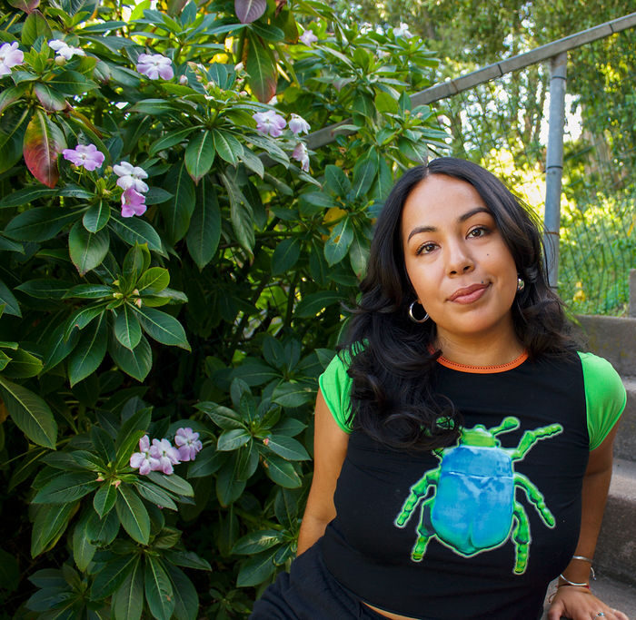 a Latina woman smiles at the camera, wearing an insect shirt