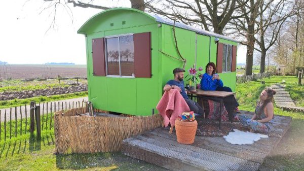 Drie mensen zitten op het terras van pipowagen Doe Maar Groen op Camping Fiederels