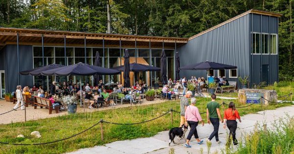 Een groepje mensen loopt met een hond langs het terras van Het ProefLab// in het Waterloopbos