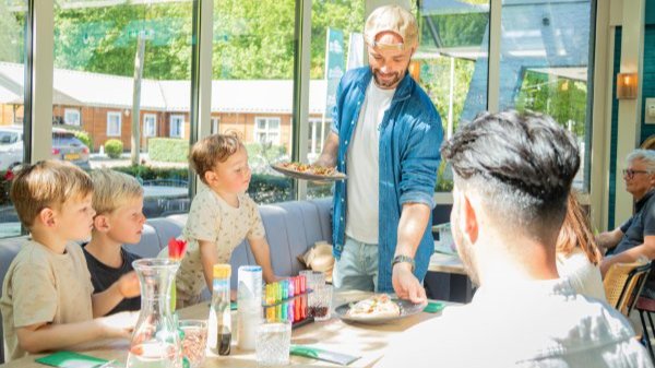 Een man serveert eten aan een gezin met jonge kinderen in het restaurant van Buitengewoon De Voorst