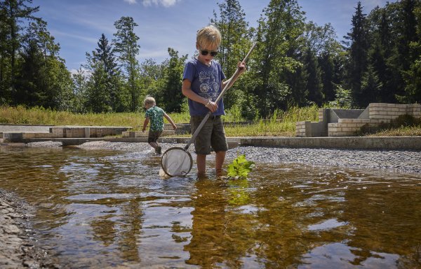 Twee kinderen zoeken naar waterdiertjes in het Waterloopbos