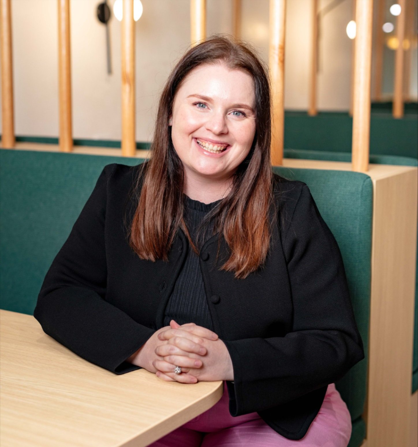 Emma Schwebel photo sitting in a booth with her hands folded together on a table. 