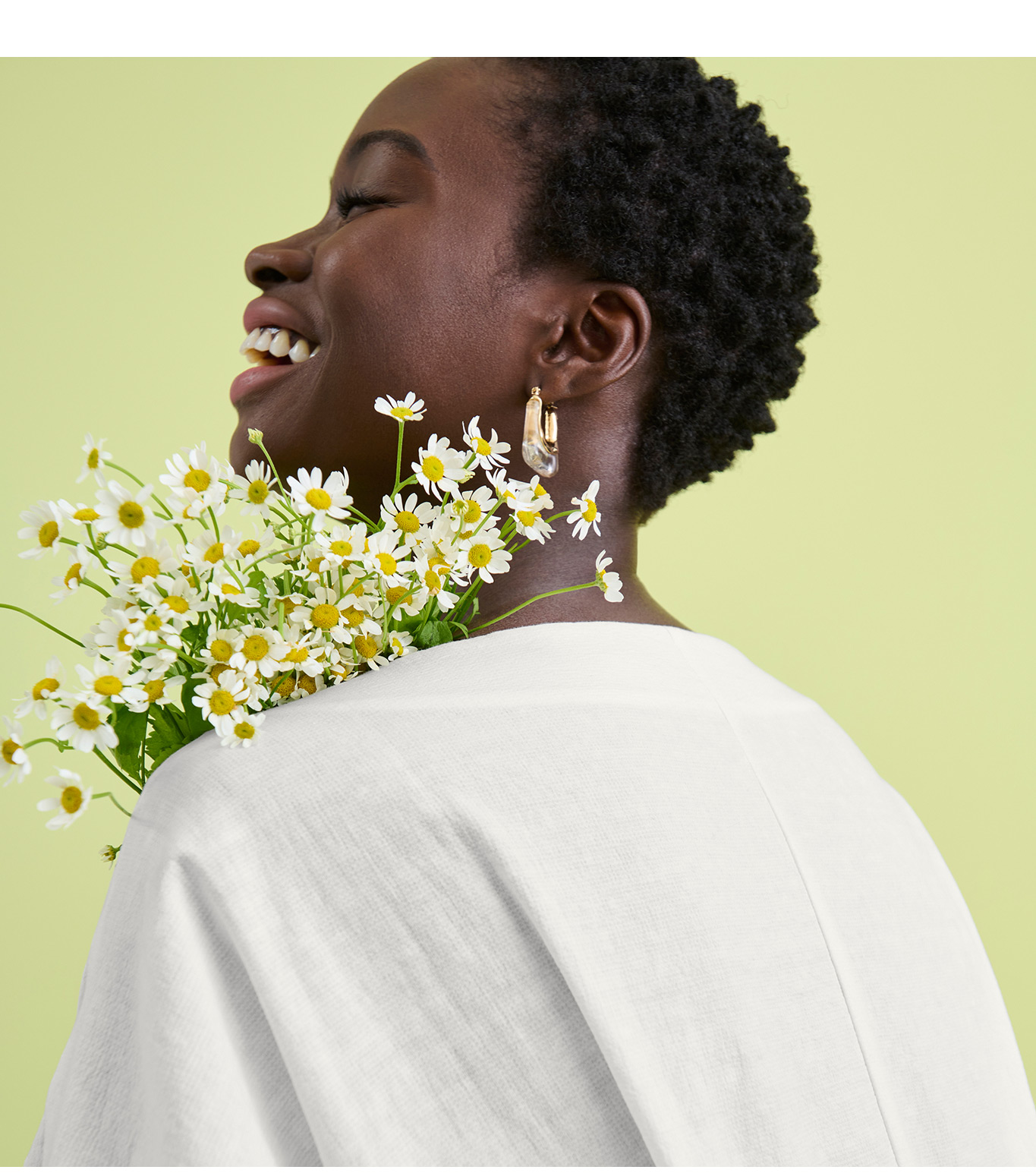 Image of a laughing woman holding a bouquet of daises and wearing a white linen top.