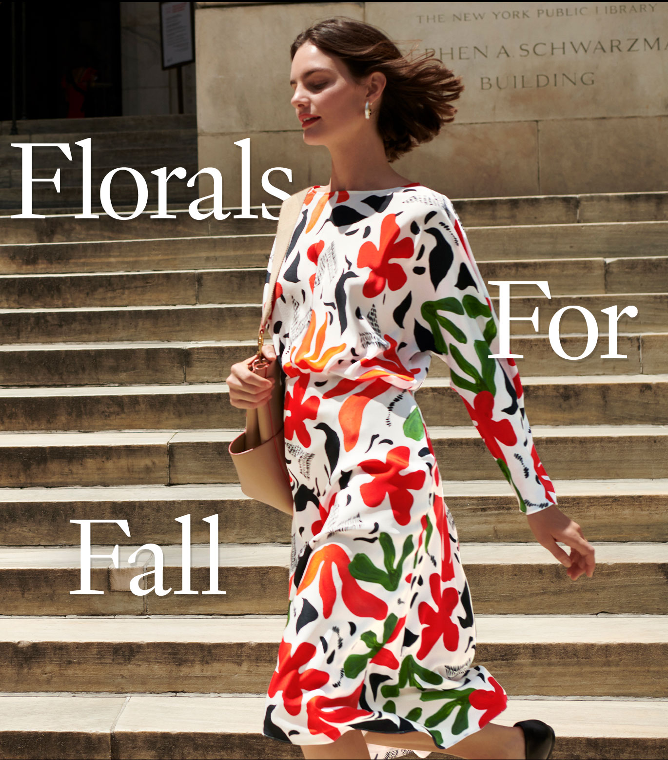 A tall woman with short brown hair walks in front of the steps of the New York Public Library. She's wearing a long flowy skirt and matching long-sleeve top, both in a multi-color floral print against a white background, and carrying a tan purse. The words ''Florals For Fall'' are overlayed on the image around the woman.