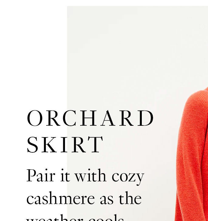 A tall brunette woman wears a long flowy skirt in a multi-color floral print on a white background paired with an orange sweater. Black text reads ''The Orchard Skirt. Pair it with cozy cashmere as the weather cools. Shop now.'' An arrow points to the orange sweater and black text reads ''Cutout print pairs perfectly with our joyful papaya color.''