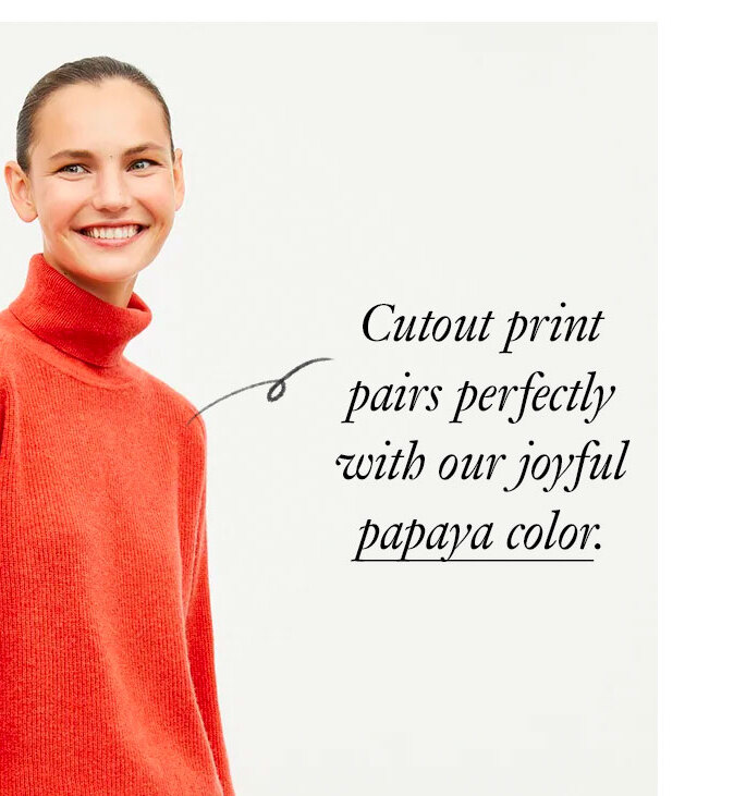 A tall brunette woman wears a long flowy skirt in a multi-color floral print on a white background paired with an orange sweater. Black text reads ''The Orchard Skirt. Pair it with cozy cashmere as the weather cools. Shop now.'' An arrow points to the orange sweater and black text reads ''Cutout print pairs perfectly with our joyful papaya color.''