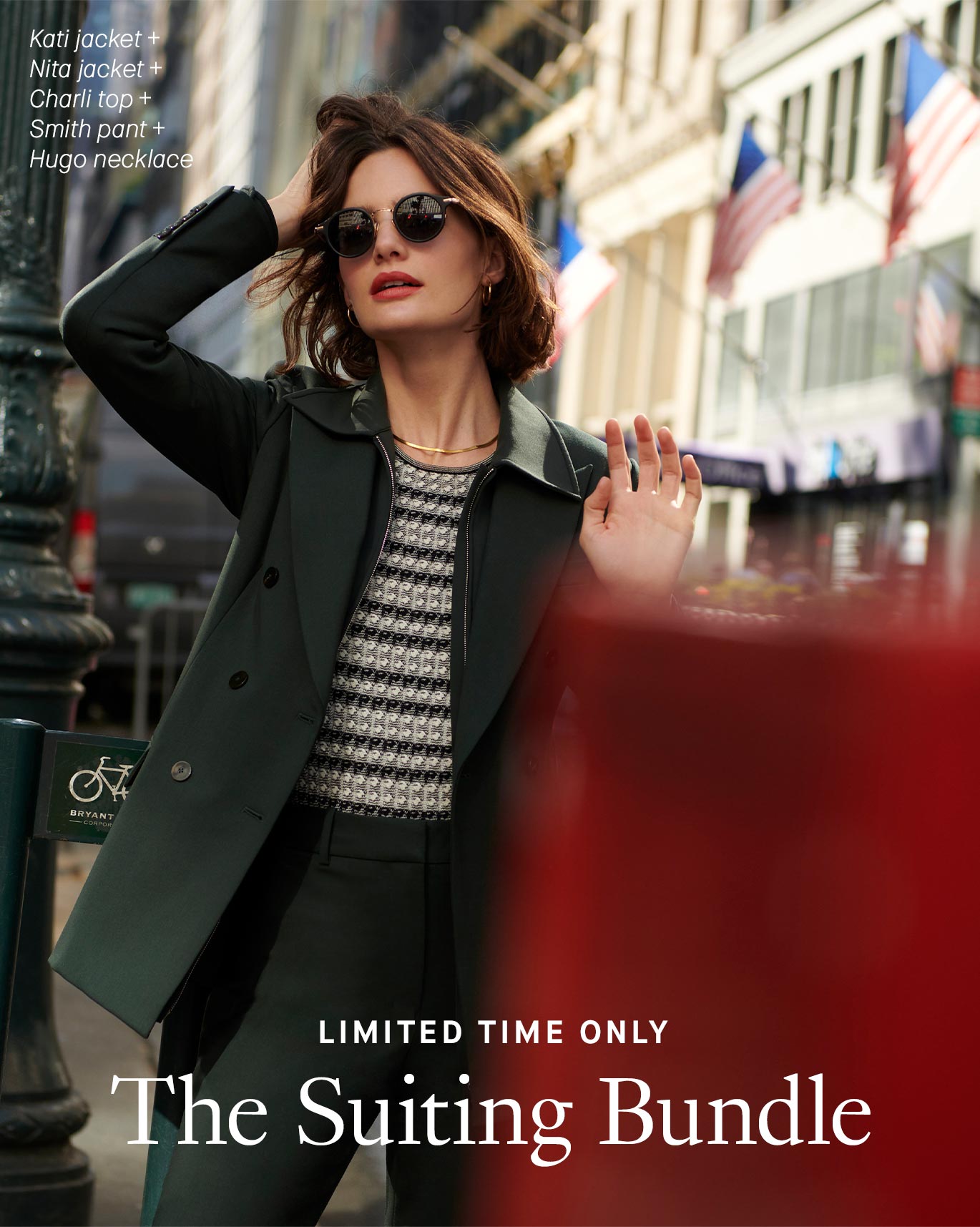 Image of a woman with short brown hair standing in a busy area of New York City with her right hand on her head and her left hand out in front of her. She's wearing dark green pants and a matching jacket with a black-and-white striped shirt underneath, accessorized with dark sunglasses and a gold necklace and earrings. A white text overlay reads ''Limited Time Only: The Suiting Bundle.'' More white text lists the items the woman is wearing: the Kati jacket, Nita jacket, Charli top, Smith pant, and Hugo necklace.