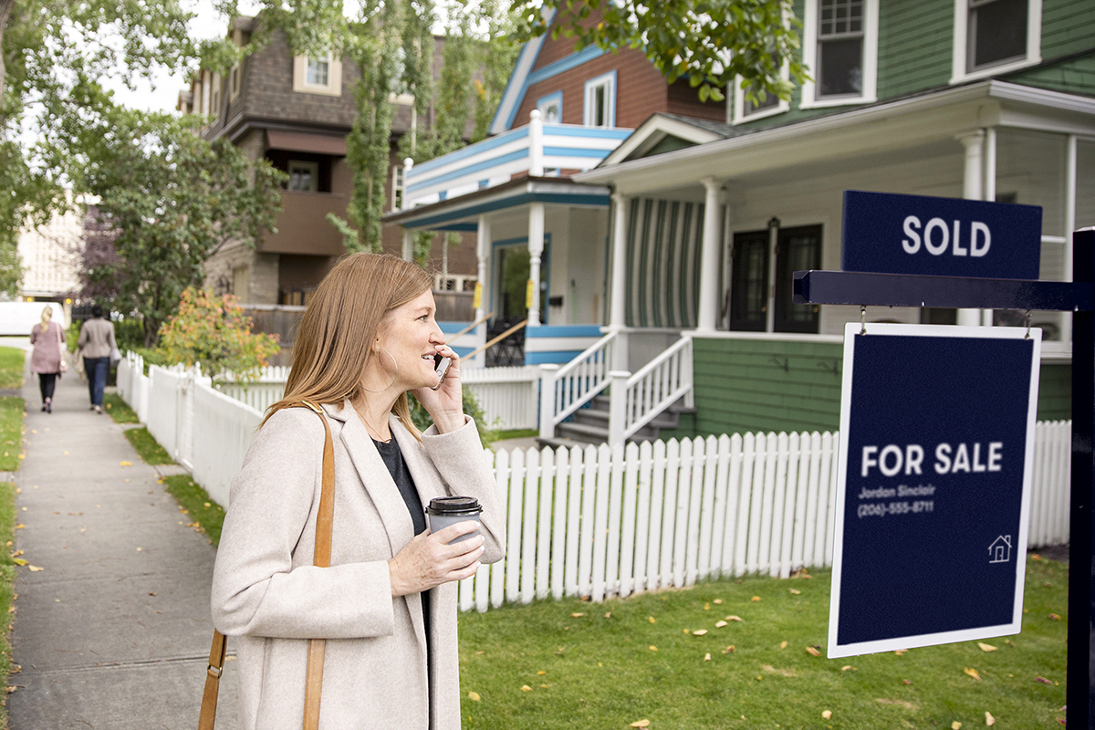 women on her cellphone standing outside a house that's for sale