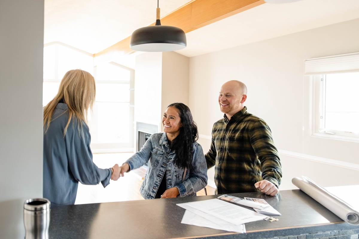 two people shaking hands over signed paperwork with a third person smiling