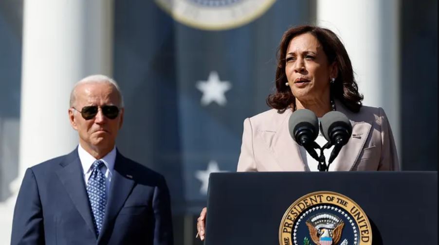 Kamala Harris speaking with Joe Biden in the background 