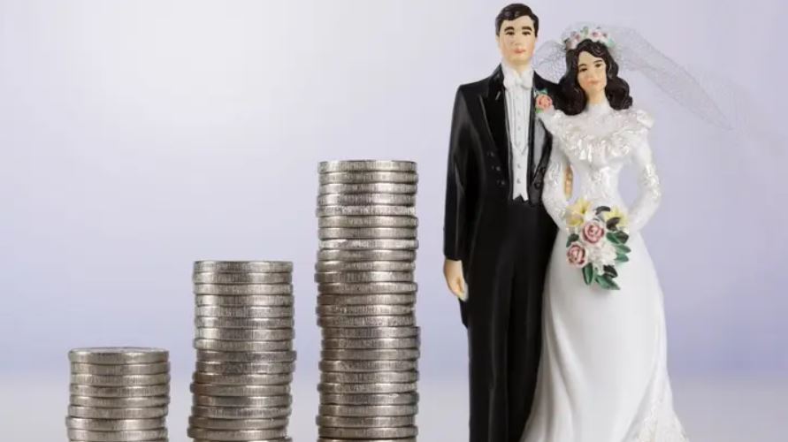 Bride and groom figurine next to stacks of coins