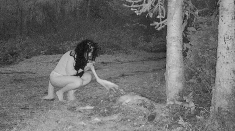 A woman on a trail camera squatting next to a dead deer