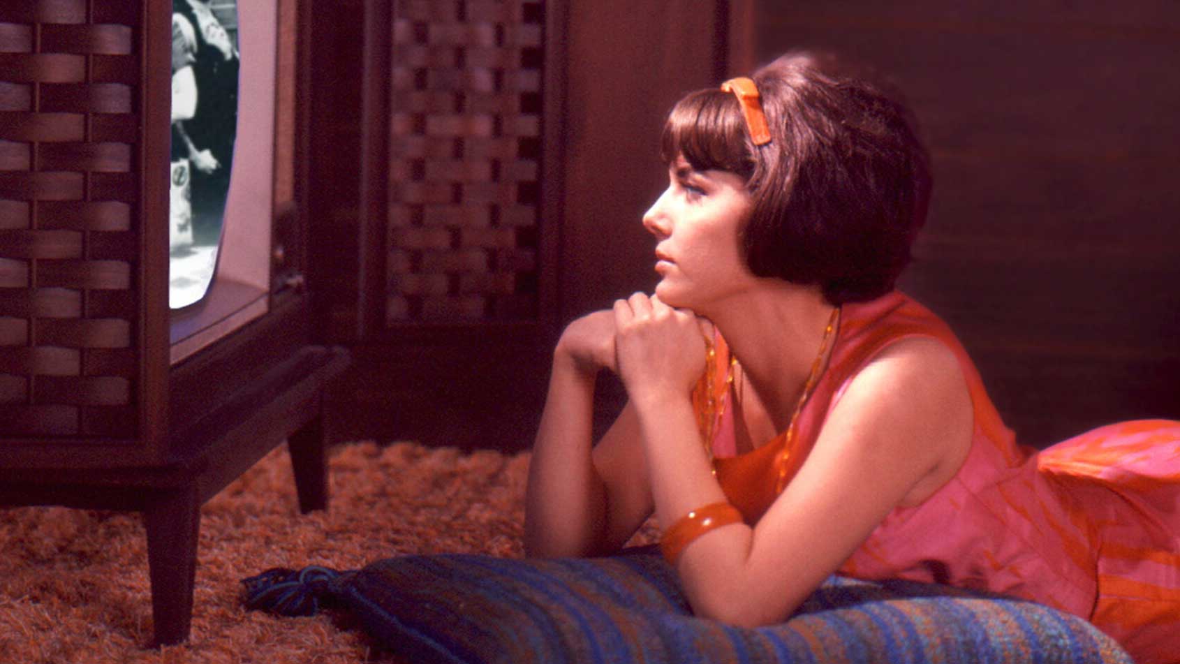 A woman lounging on the ground looking at a TV screen