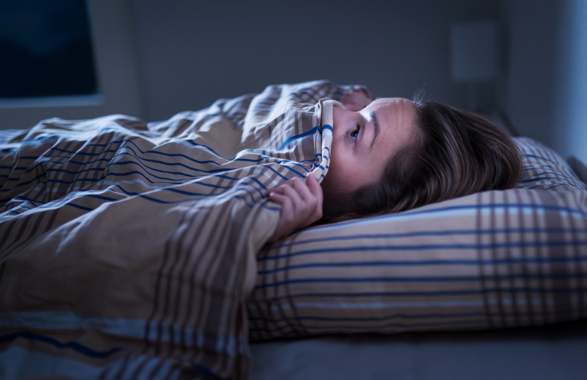 Person in bed looking out from under the covers