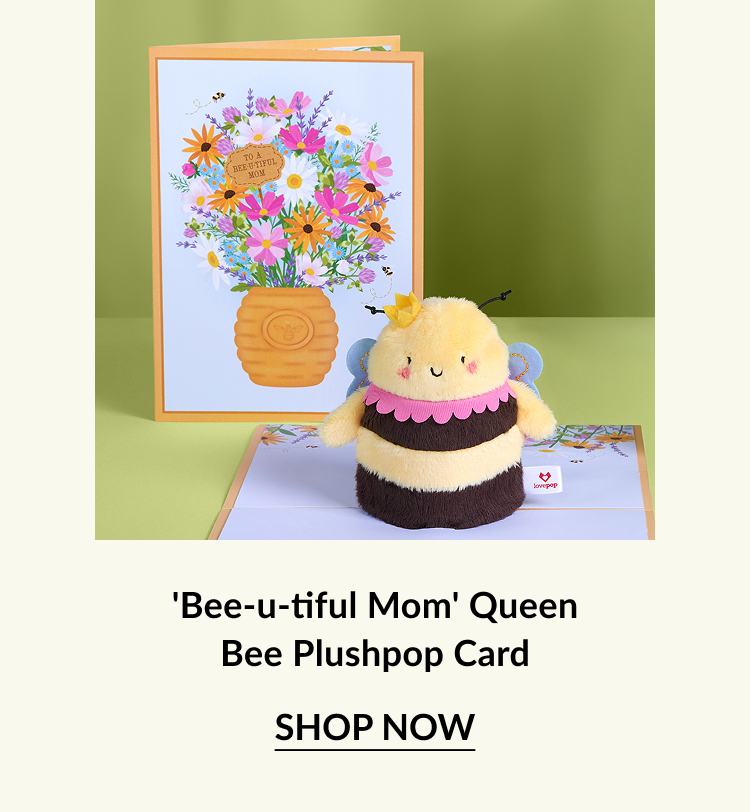 A cute bee plush toy in front of a colorful card that reads ''To a Bee-utiful Mom,'' featuring a vibrant floral design.