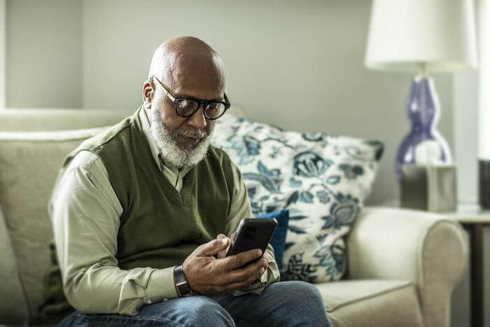 Elder adult sitting on couch looking at cell phone.