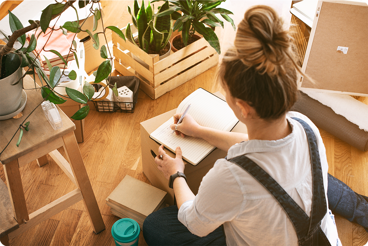 a woman sitting on the floor among moving boxes, making a budget.