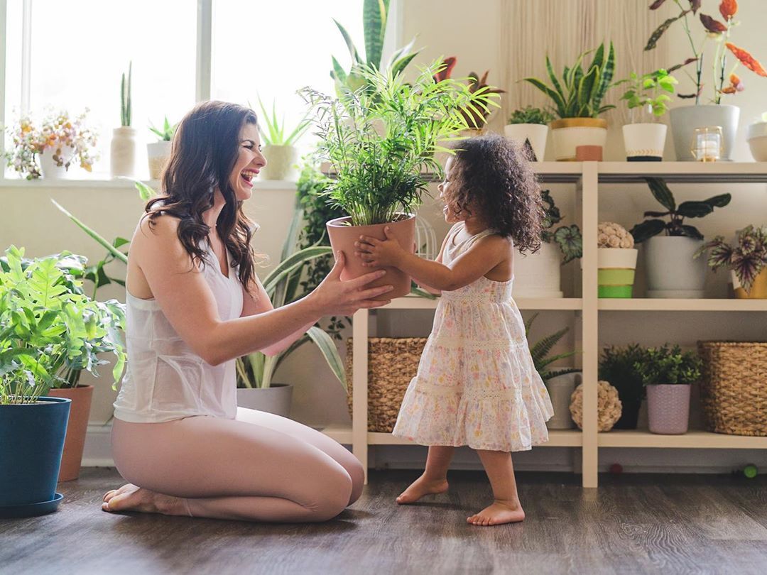 Bloomscape ambassador and mother @alexiskristiana kisses her baby's hand in front of a Bird of Paradise and Bamboo Palm
