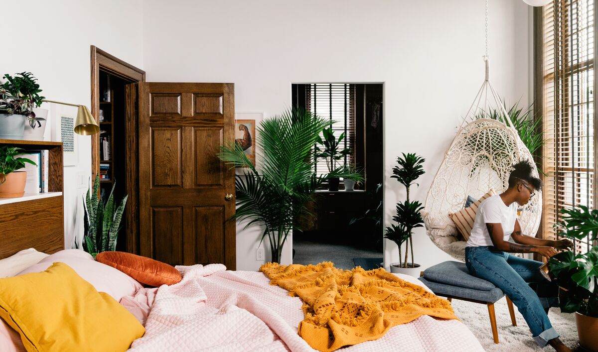 Woman admiring her Monstera plant in a plant-filled bedroom