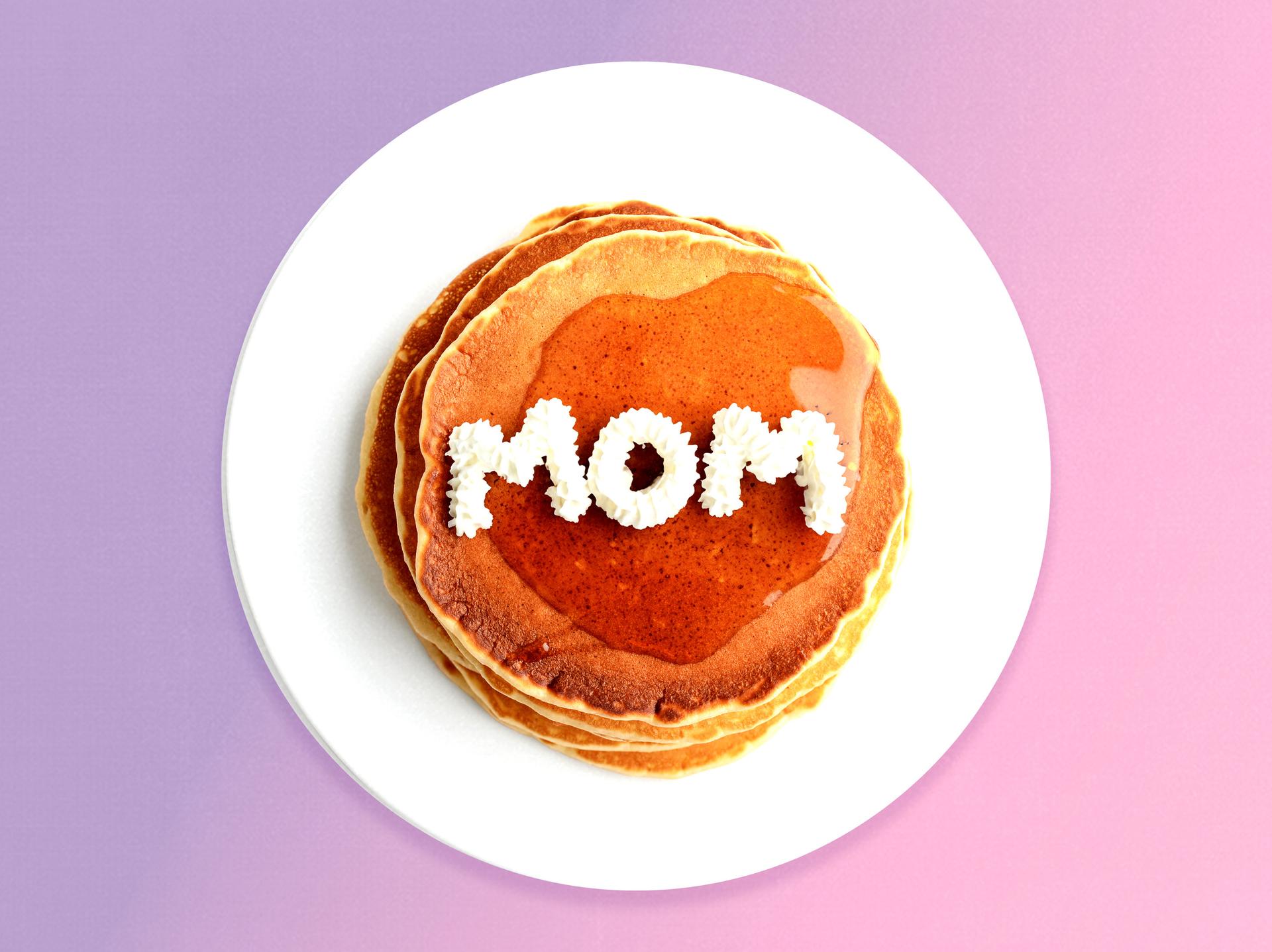 A stack of pancakes with ''mom'' written in whipped cream on top of them.