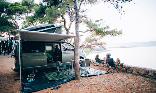Couple sitting in front of camper van by lake