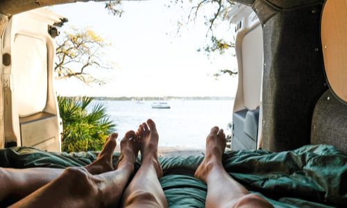 People laying in camper with open door in front of lake