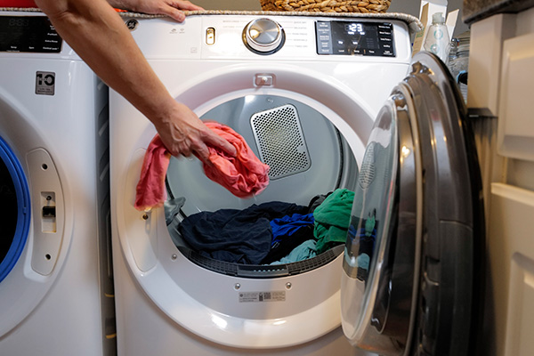 Person loading clothes into frontload dryer.