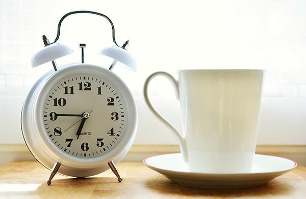 White analog alarm clock sitting next to mug on saucer.