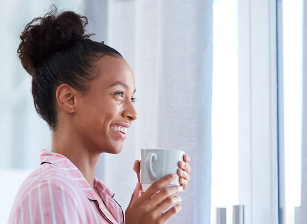 Smiling woman staring out window, holding mug.