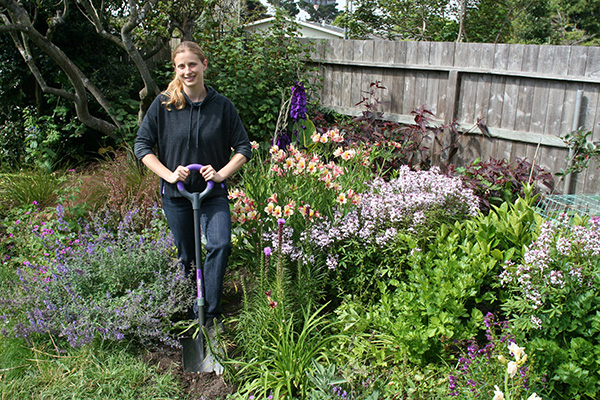 Blonde woman digging with shovel in outdoor flower patch.