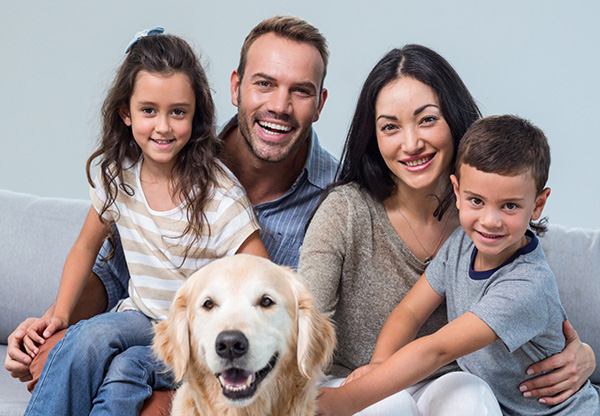 Smiling family of four sitting on couch with golden retriever.