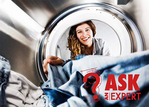 Woman with long, curly brown hair smiling while unloading a clothes dryer.